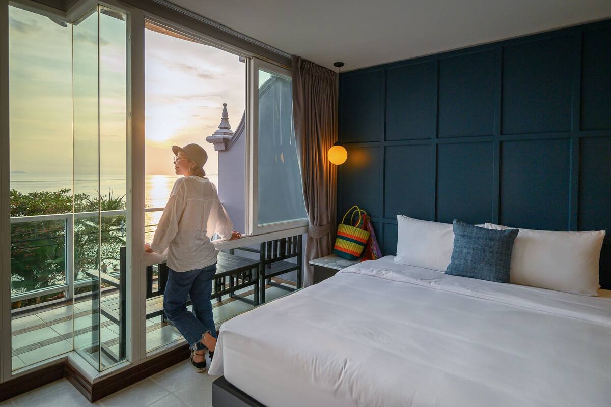 A hotel room with a large window, a bed, and a view of the sunset.