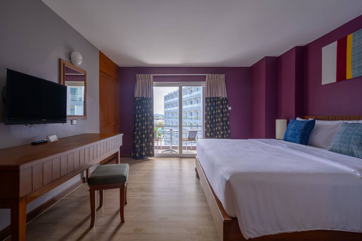A hotel room with a bed, a desk, a chair, a TV, and a balcony with curtains.