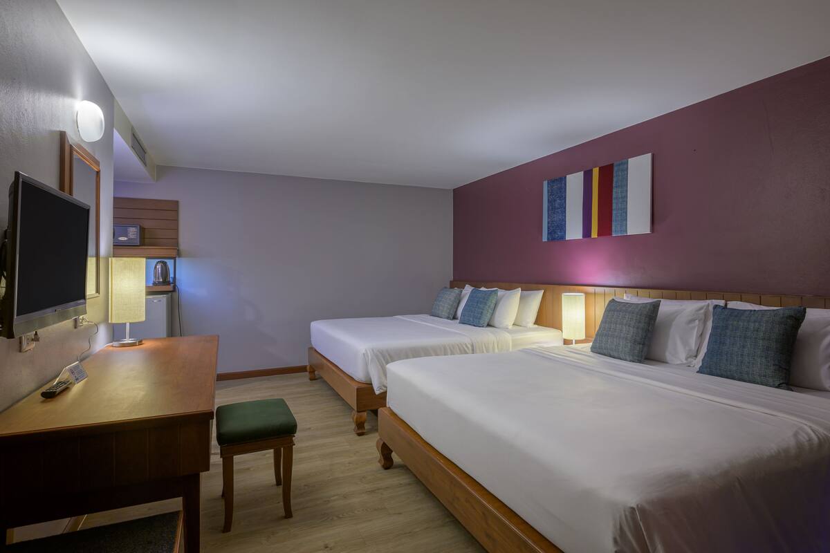 A hotel room with two beds, a desk with a chair, a television, and a wall-mounted artwork.