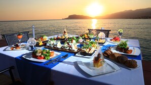 A table set for a meal with various dishes and drinks, overlooking a body of water at sunset. - LABRANDA Alantur Resort - All Inclusive (Alanya)