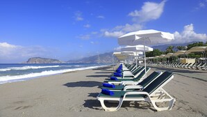 A beach with rows of sun loungers under umbrellas, a clear sky, and a view of the sea and distant mountains. - LABRANDA Alantur Resort - All Inclusive (Alanya)