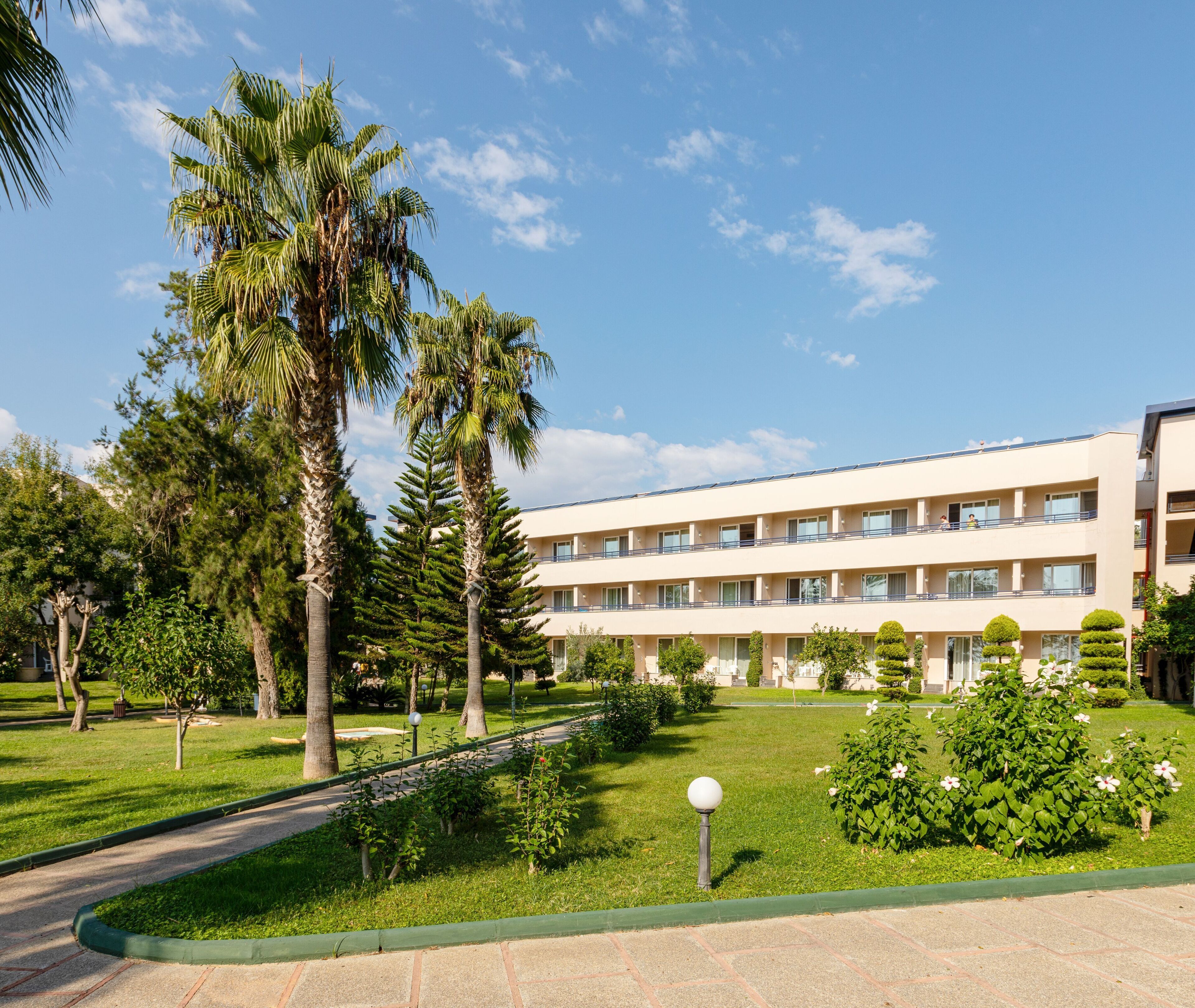 Um hotel com vários andares e um pátio central, rodeado por palmeiras e vegetação bem cuidada.