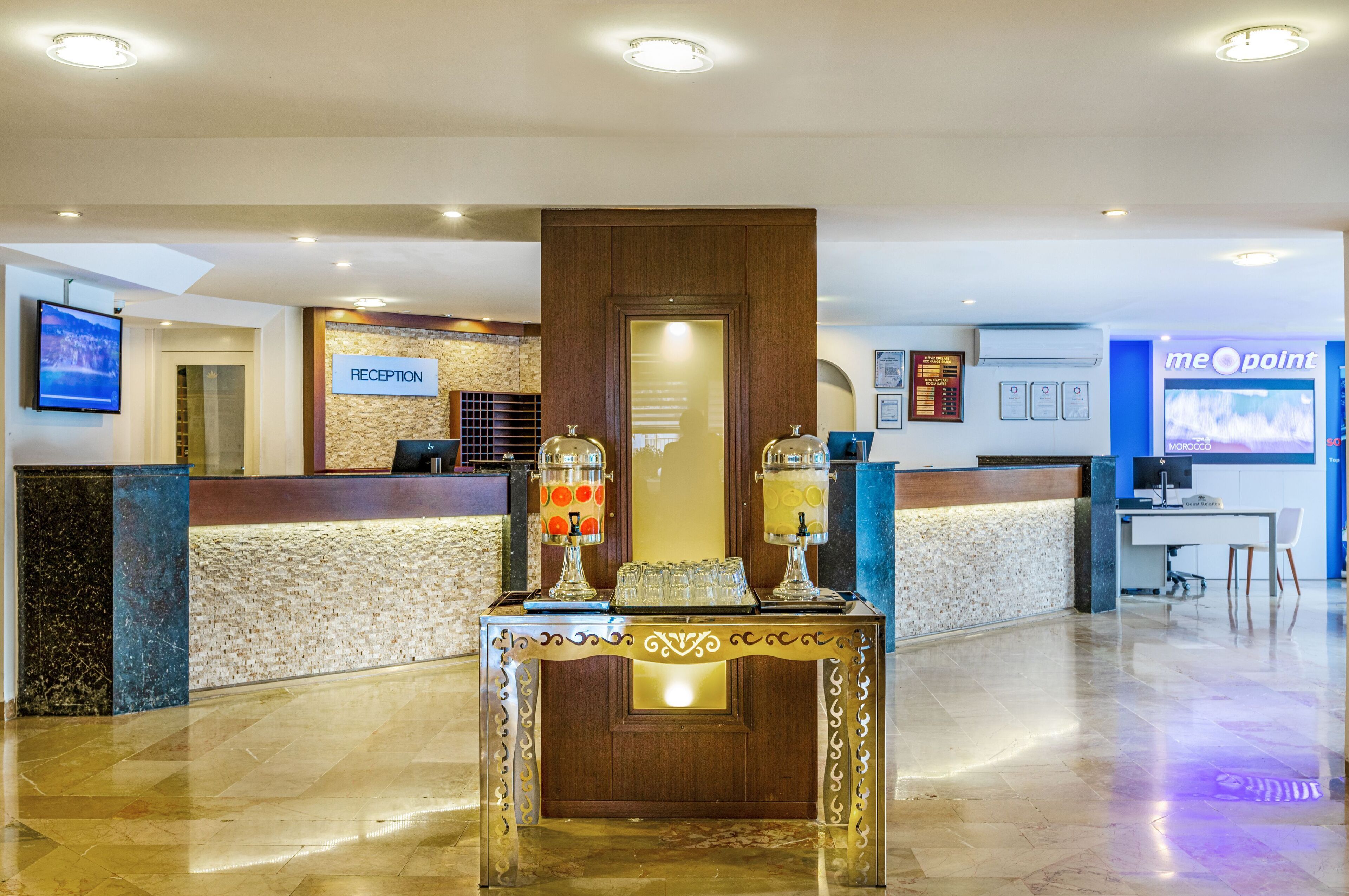 A reception area with a reception desk, a wall-mounted TV, and a glass display case with a beverage dispenser.