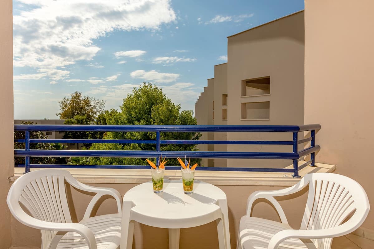 A balcony with two white plastic chairs, a small round table, and two glasses of a drink with a straw.