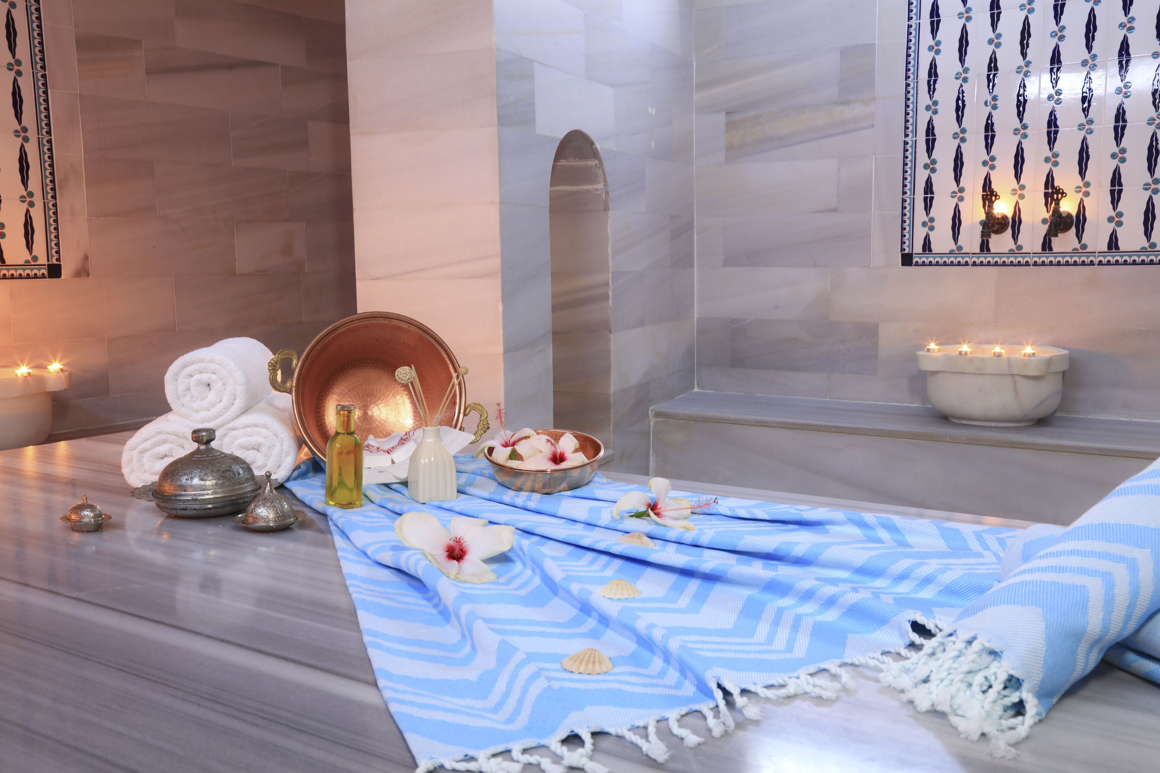 A spa area with a wooden floor, a blue patterned towel, a bowl of fruit, a metal container, and a white candle holder.