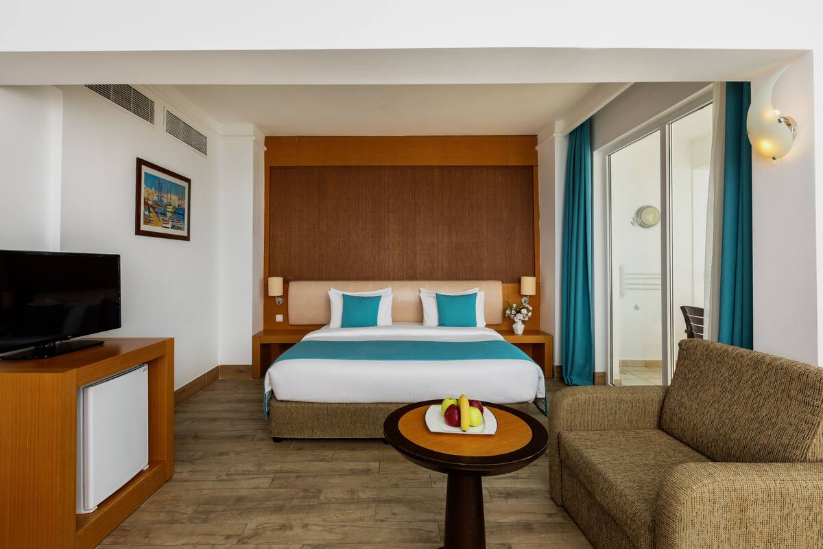 A hotel room with a bed, a television, a small table with fruit, and a sofa.