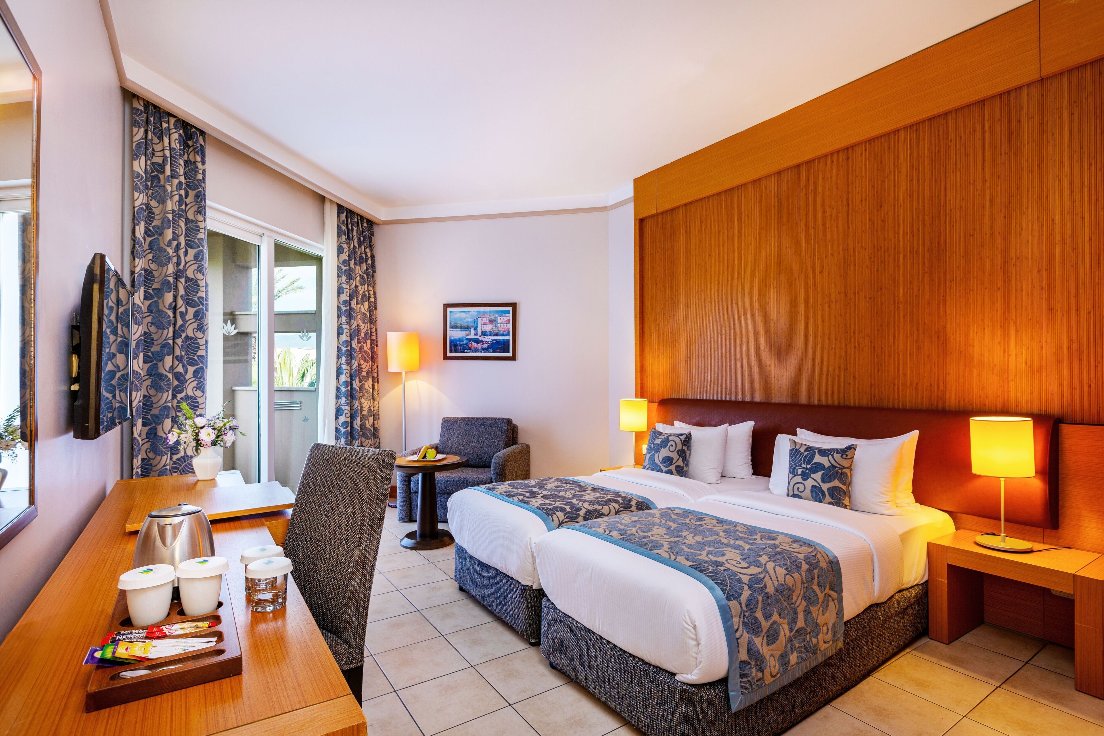 Hotelkamer met twee bedden, een bureau met koffiezetapparaat, een stoel en een tafel met ontbijtartikelen.