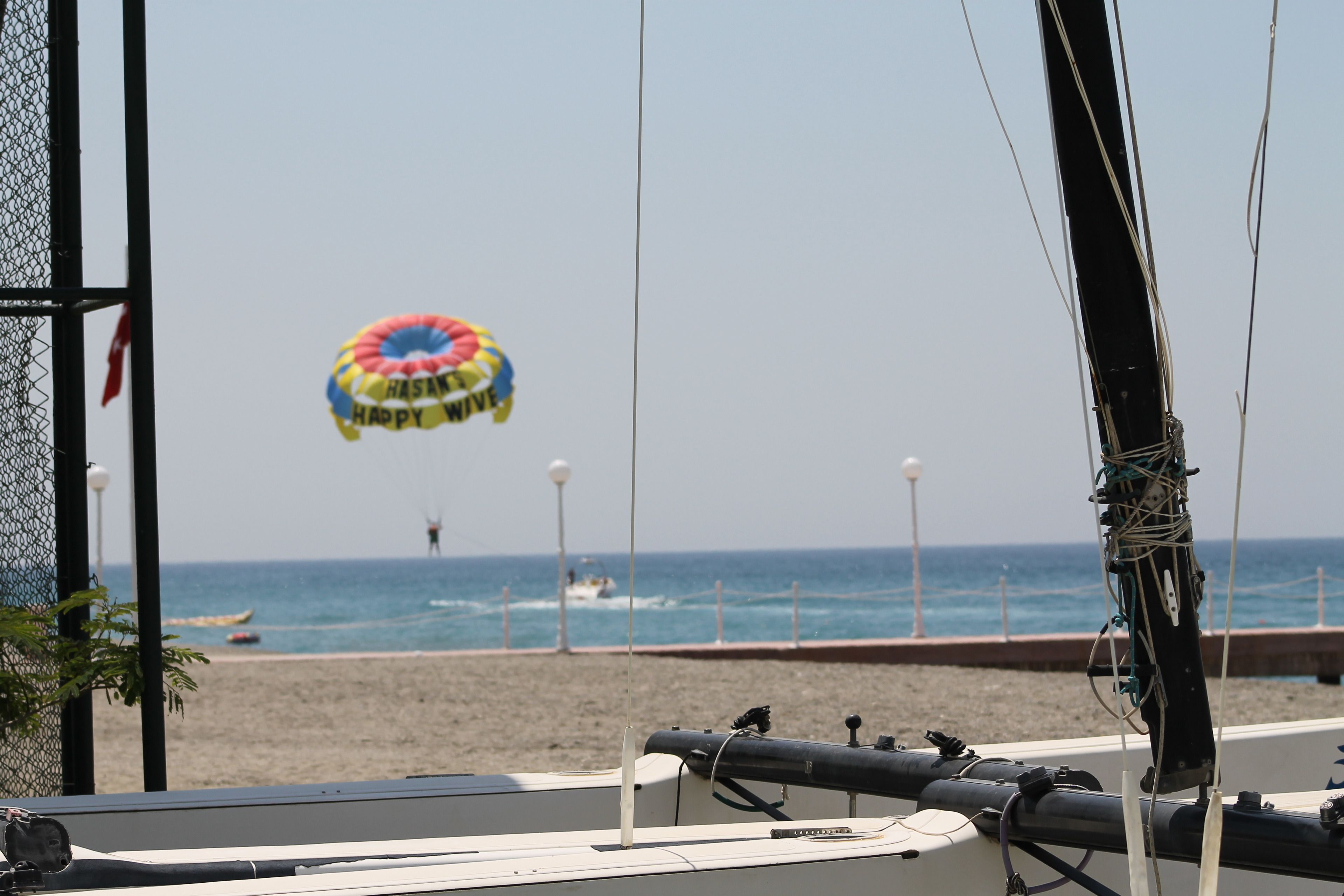 A beach view with a parasail in the distance, a boat docked nearby, and a clear sky.