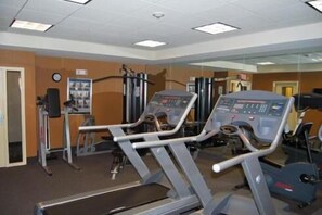 Een fitnessruimte met loopbanden, krachttoestellen en een spiegelwand.