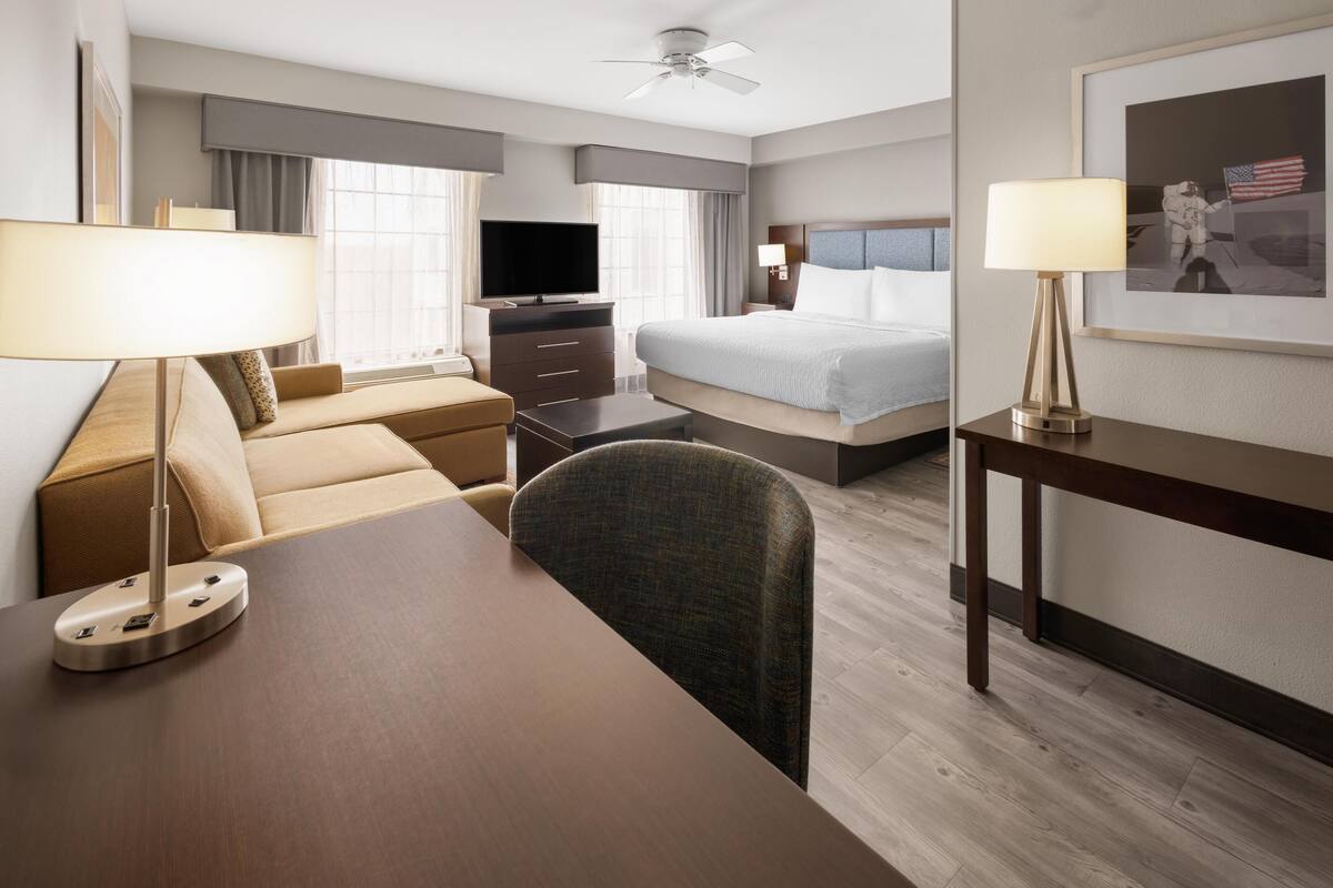 Une chambre d’hôtel équipée d’un lit, d’un bureau, d’une télévision et d’un ventilateur de plafond.