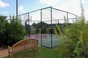 Een basketbalveld omgeven door een net, met een bank en begroeiing eromheen.