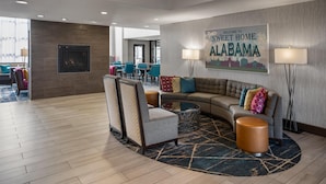Een moderne hotellobby met een gebogen bank, fauteuils en een eetgedeelte op de achtergrond.