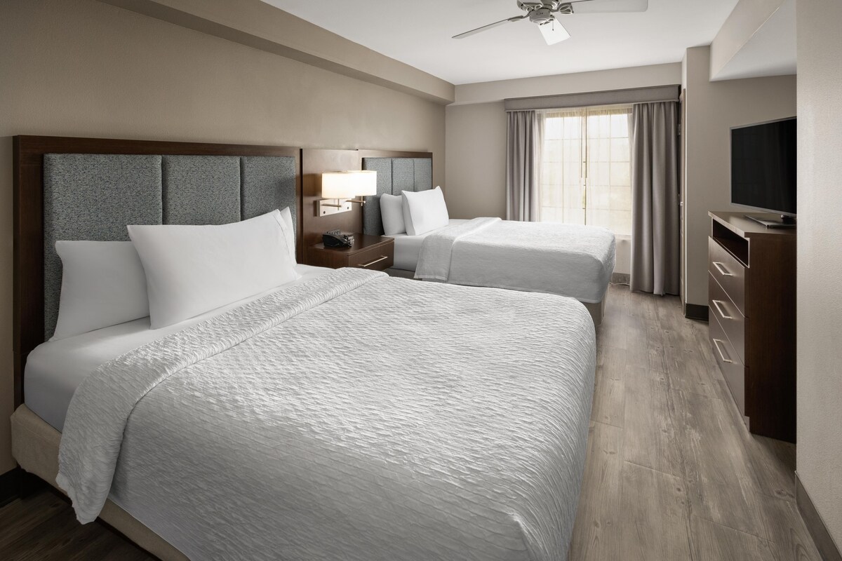 Een hotelkamer met twee bedden, een bureau, een televisie en een plafondventilator.