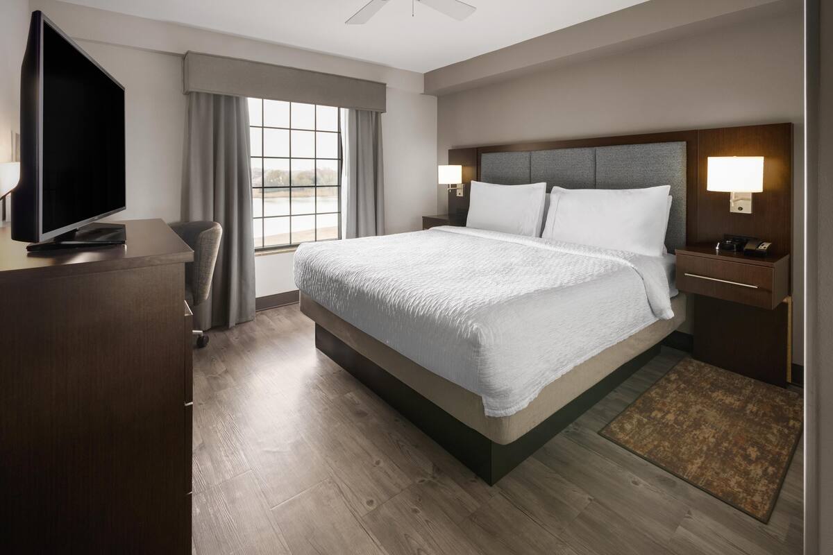 Une chambre d’hôtel avec un grand lit, un téléviseur à écran plat, un bureau et une fenêtre avec des rideaux.