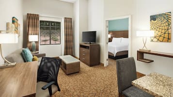A hotel room with a bed, a desk with a chair, a television, and a small table.