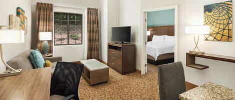A hotel room with a bed, a desk with a chair, a television, and a small table.