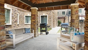 An outdoor patio area with stone walls, a barbecue grill, and seating arrangements. - Staybridge Suites Durham/Chapel Hill by IHG (Durham)