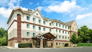 A multi-story hotel with a prominent entrance, a covered outdoor seating area, and a clear blue sky. - Staybridge Suites Durham/Chapel Hill by IHG (Durham)