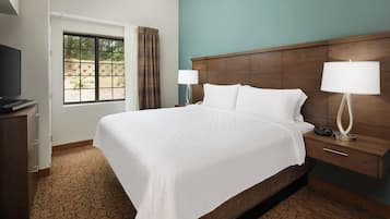 A hotel room with a large bed, a wooden headboard, a bedside table with a lamp, and a television on a stand.