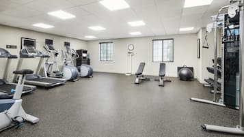Un gimnasio con cintas de correr, elípticas, una banca y equipo de levantamiento de pesas.