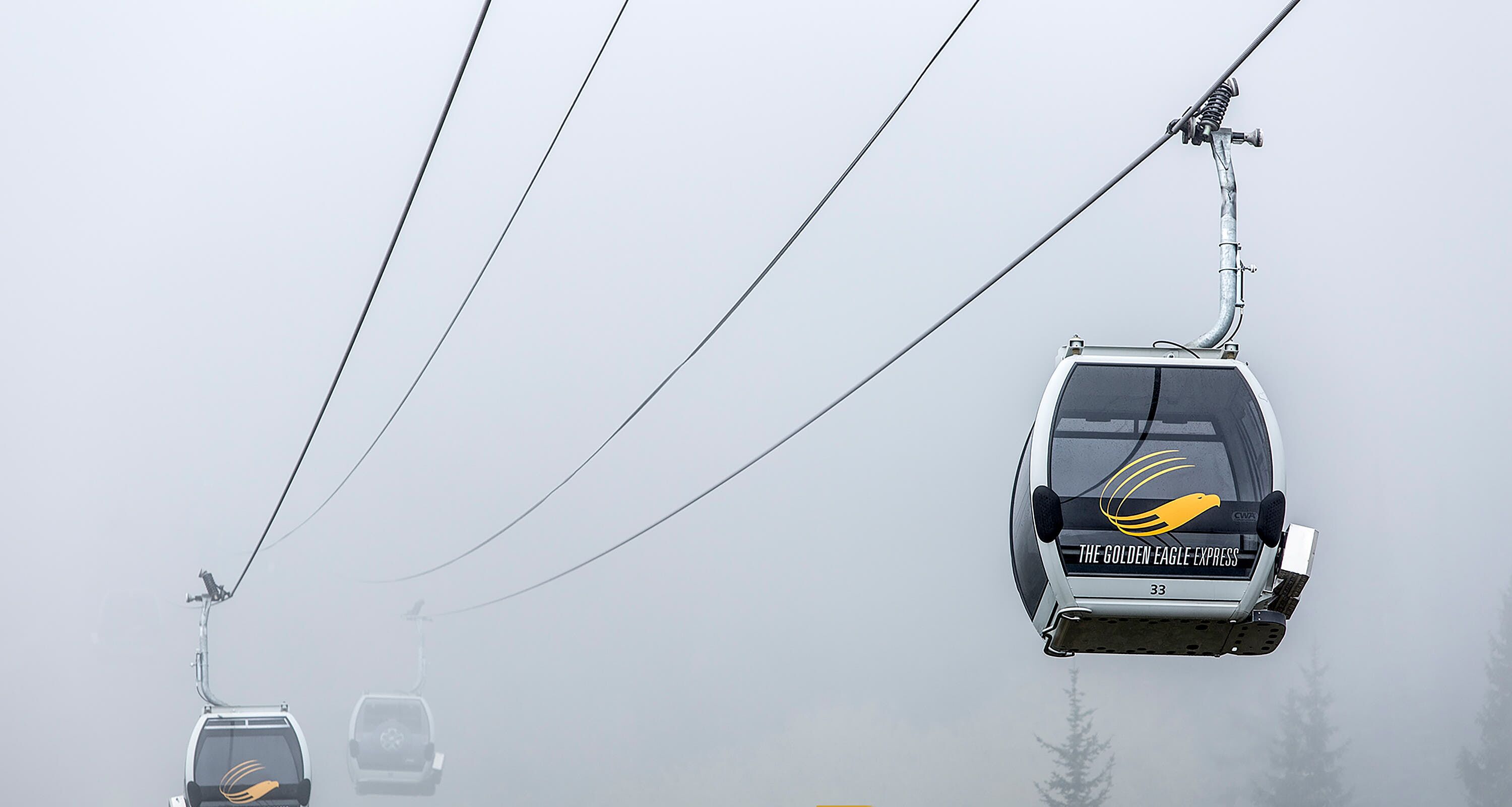A cable car with the logo "The Golden Eagle Express" suspended in foggy weather.