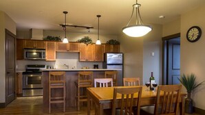 Een keuken met houten kasten, roestvrijstalen apparatuur en een eethoek met houten stoelen en een tafel.