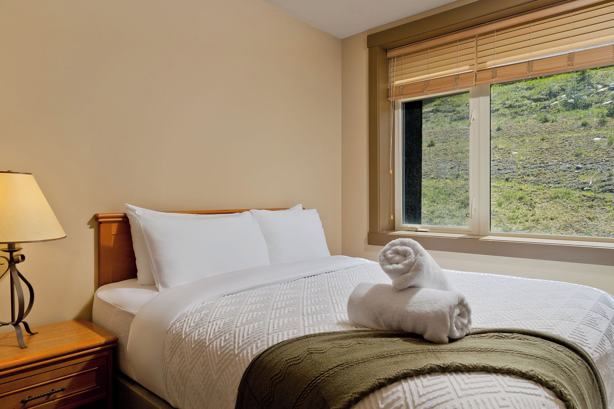 Une chambre d’hôtel avec un lit, une table de chevet, une lampe et une fenêtre donnant sur un paysage verdoyant.