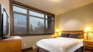 Hotelkamer met een groot bed, twee bedlampen, een televisie op een standaard en een raam met jaloezieën.