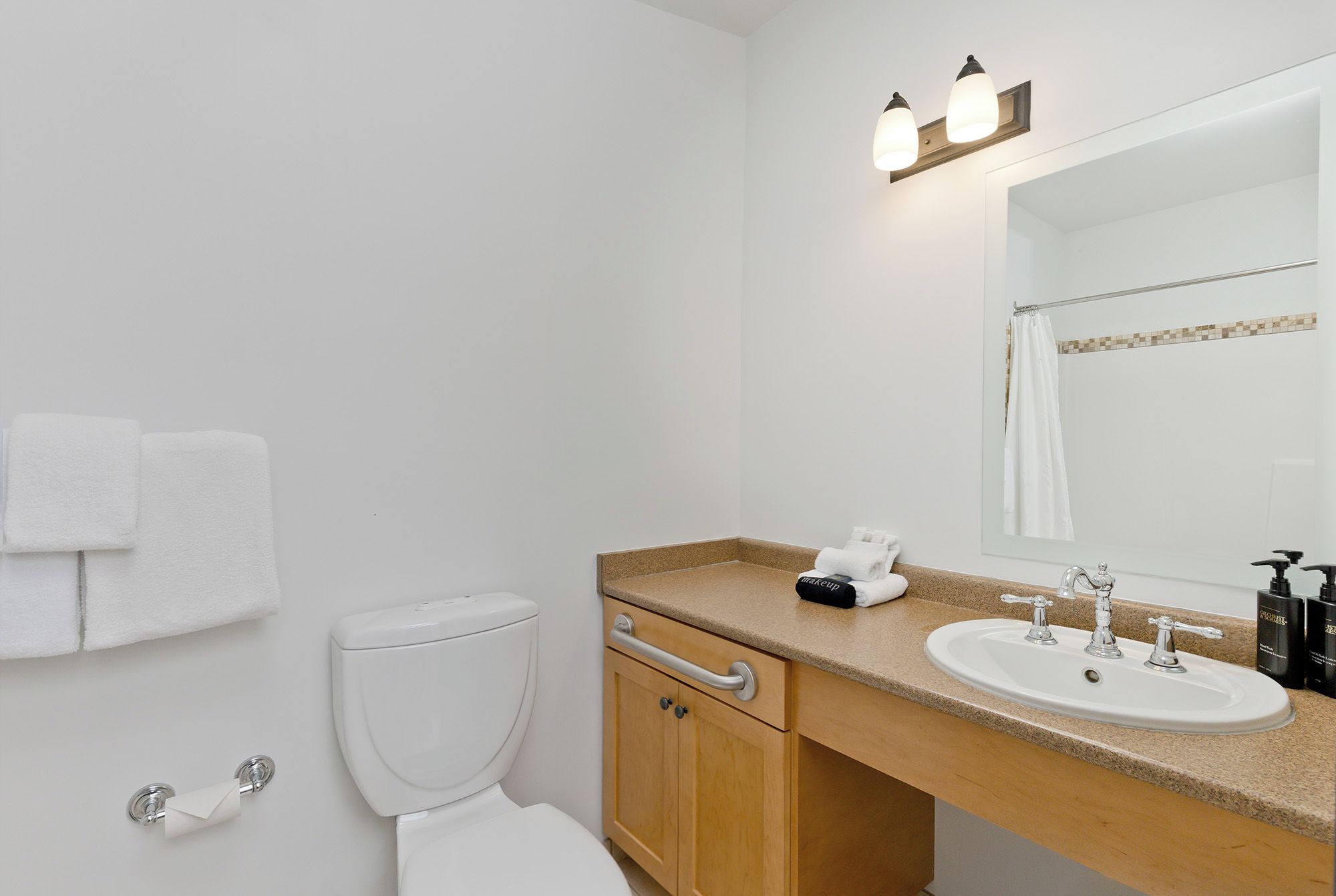 A bathroom with a toilet, sink, mirror, towel rack, and a towel dispenser.