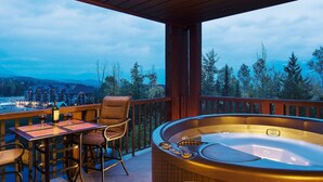 Een houten terras met een jacuzzi, een tafel met stoelen en uitzicht op een berglandschap.