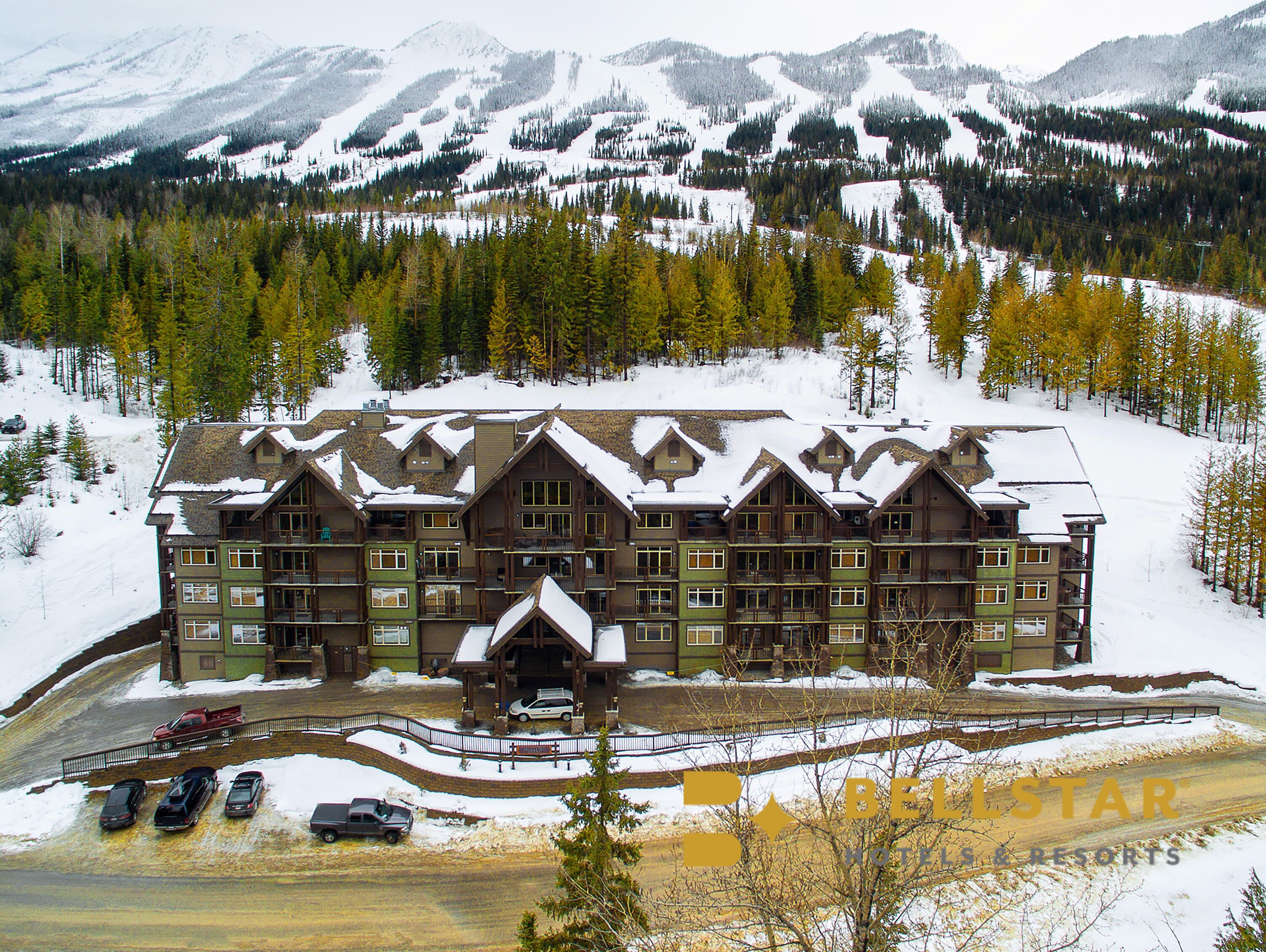 Un gran lodge con varios balcones y un acceso cubierto, rodeado de montañas y árboles nevados.