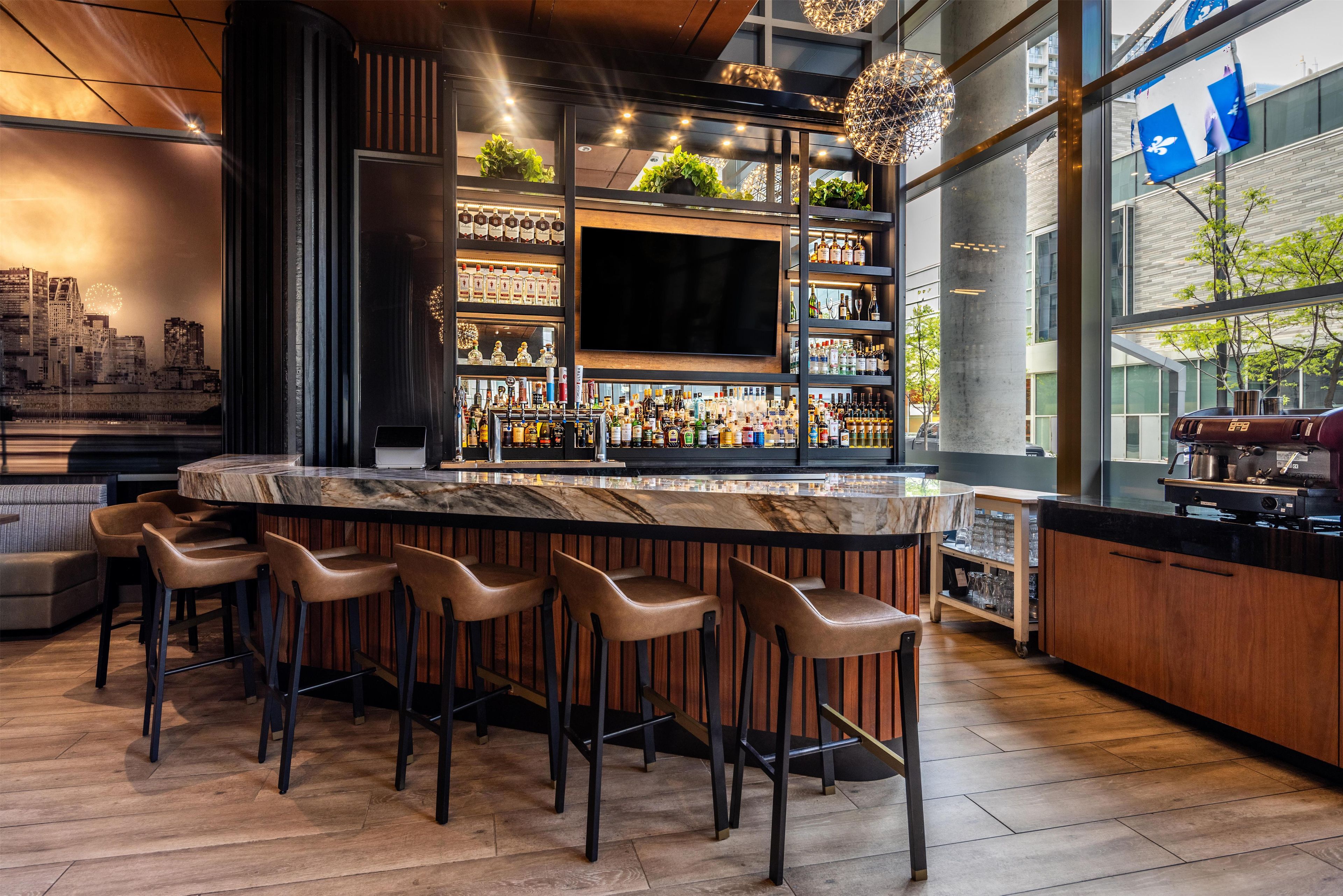 A bar area with a marble countertop, multiple bar stools, and a variety of bottles and glasses.
