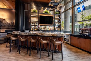 A bar area with a marble countertop, multiple bar stools, and a variety of bottles and glasses. - Embassy Suites Montréal by Hilton (Montreal)