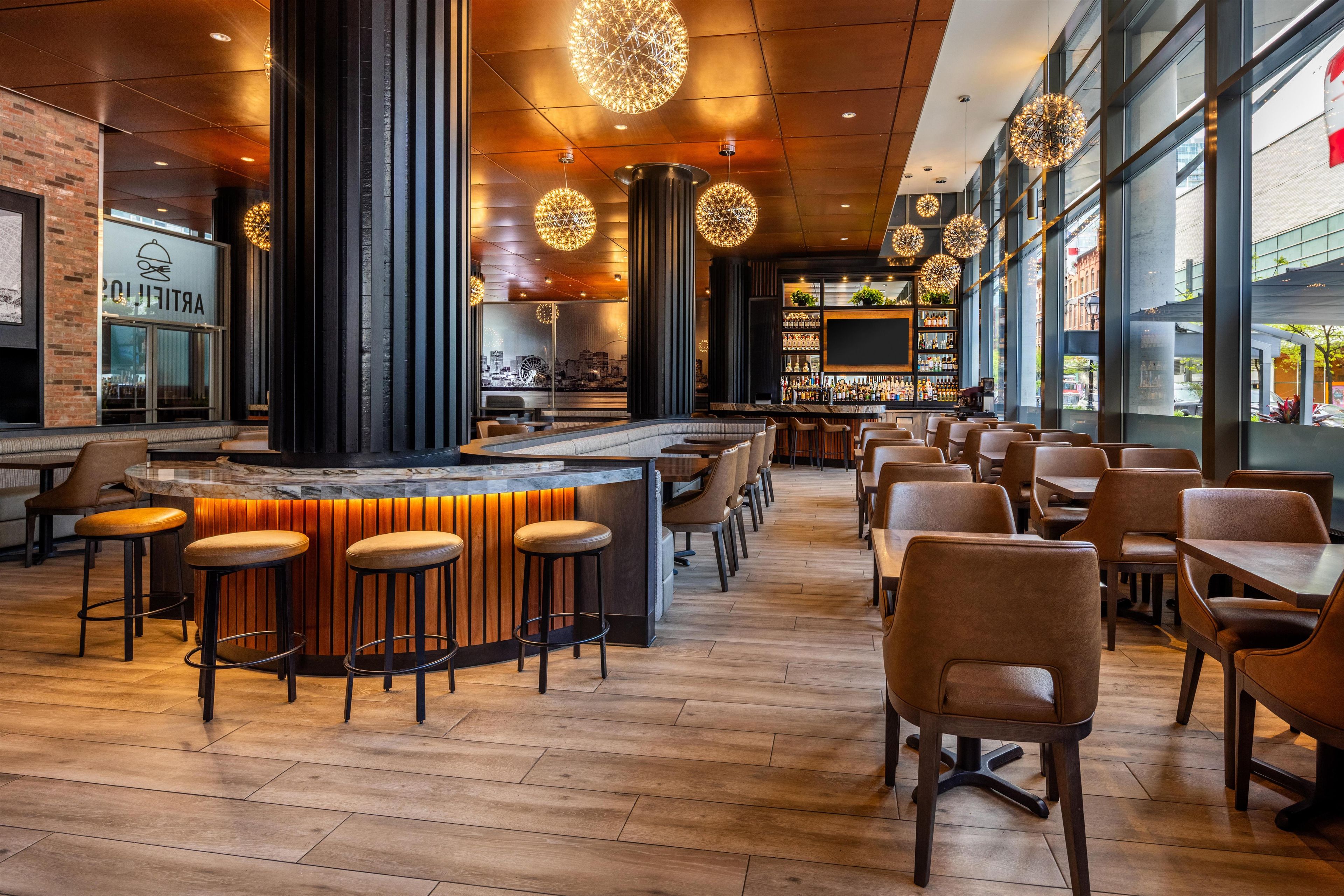A modern bar area with high stools, a central bar counter, and a city view through large windows.