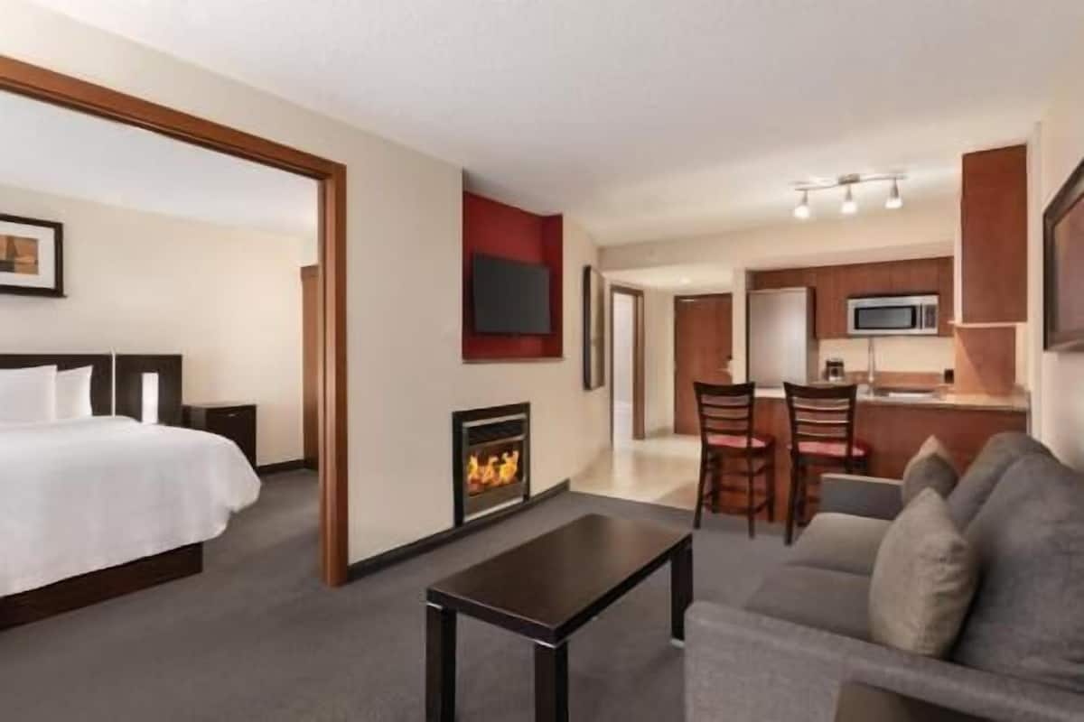 A hotel room with a bed, a fireplace, a dining area with chairs, and a kitchen area with a microwave.