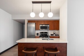 A modern kitchen with a central island, stainless steel appliances, and wooden cabinets. - Embassy Suites Montréal by Hilton (Montreal)