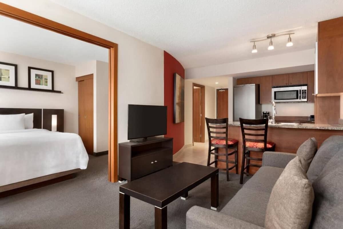 A hotel room with a bed, a TV, a small table, a sofa, and a kitchenette.