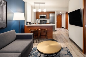 A modern hotel room with a sofa, a round table, a kitchen area with a microwave, a refrigerator, and a bar stool. - Embassy Suites Montréal by Hilton (Montreal)