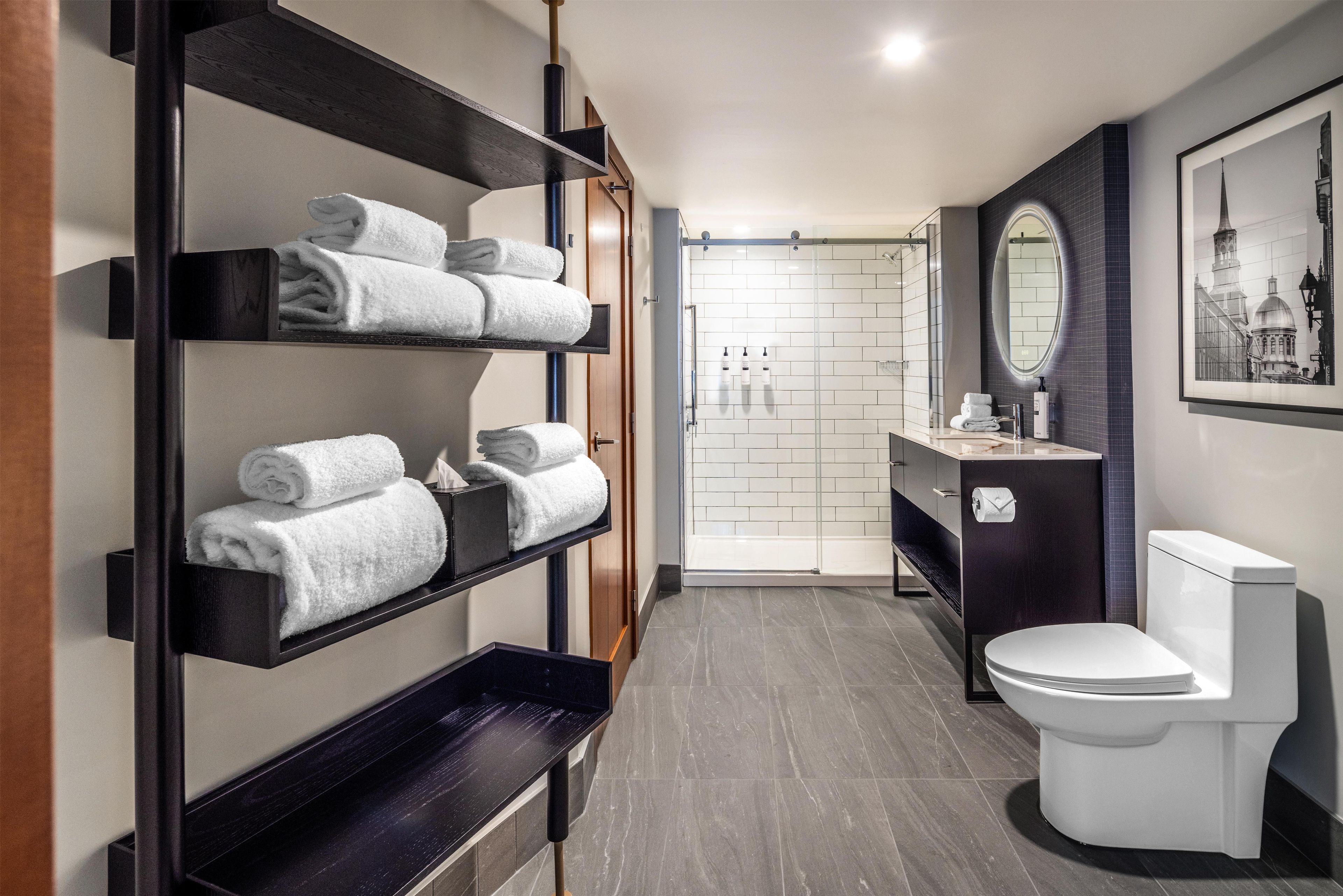 A modern bathroom with a shower, toilet, and a shelf with towels.