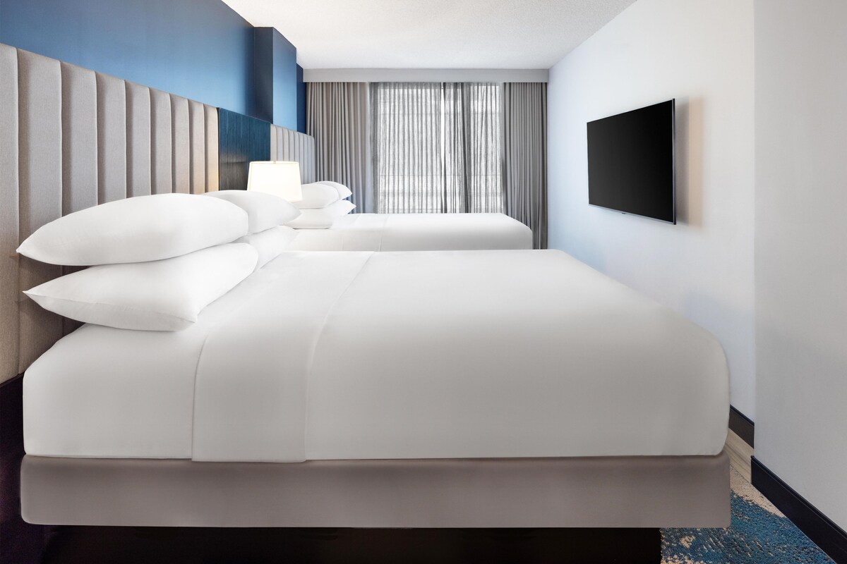 A hotel room with a large bed, a flat-screen TV, and a window with curtains.