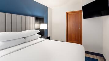 Habitación de hotel con cama, mesita de noche, lámpara, puerta de madera y televisor de pantalla plana montado en la pared.