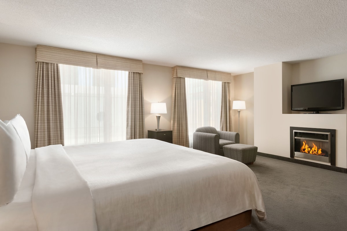 A hotel room with a large bed, two lamps, a television, and a fireplace.