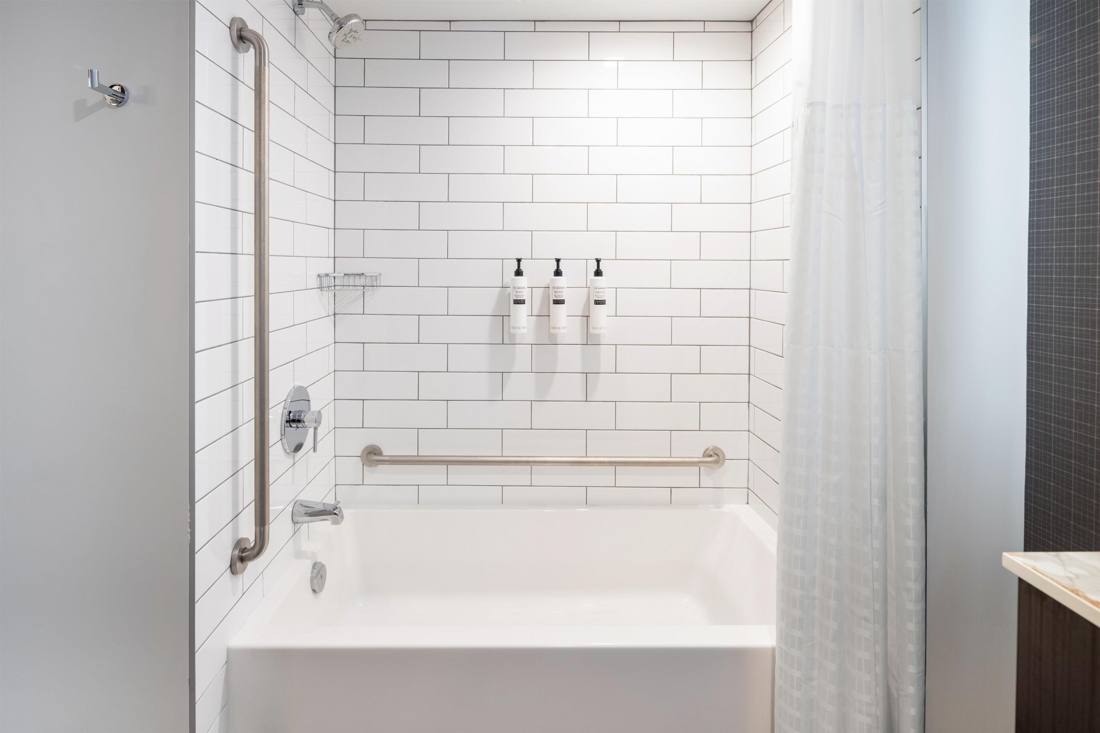 Un baño moderno con azulejos blancos tipo metro, una bañera, una ducha con cabezal de ducha manual y un perchero para toallas.