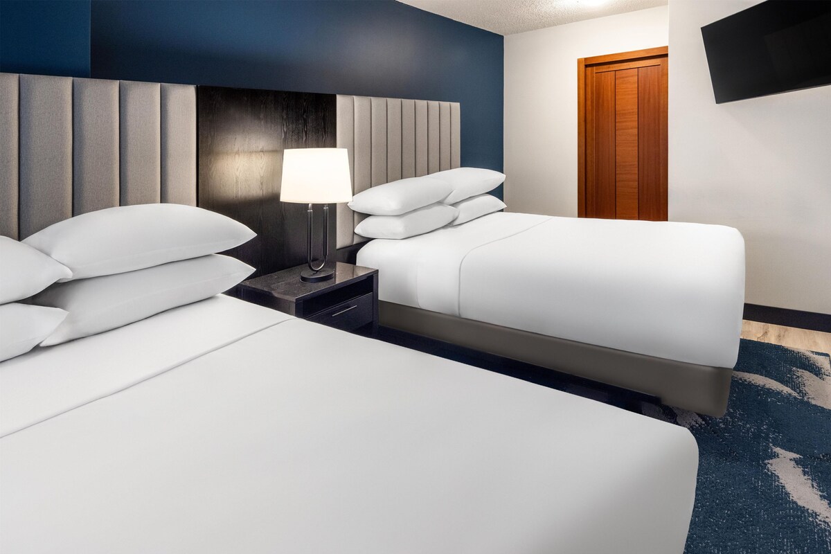 A hotel room with two beds, a nightstand with a lamp, and a wooden door.