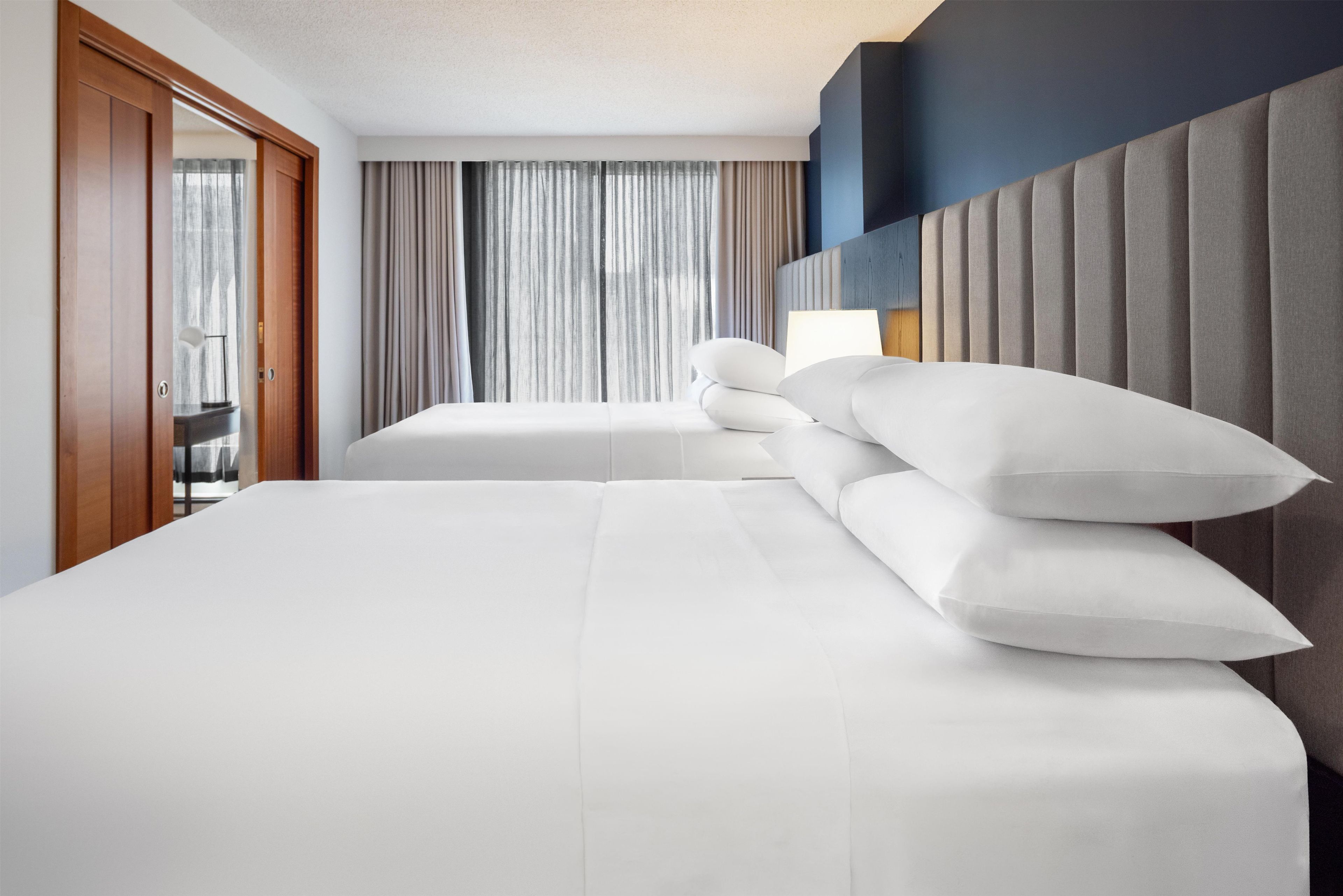 A hotel room with two beds, a wooden door, and a view of the street through the window.