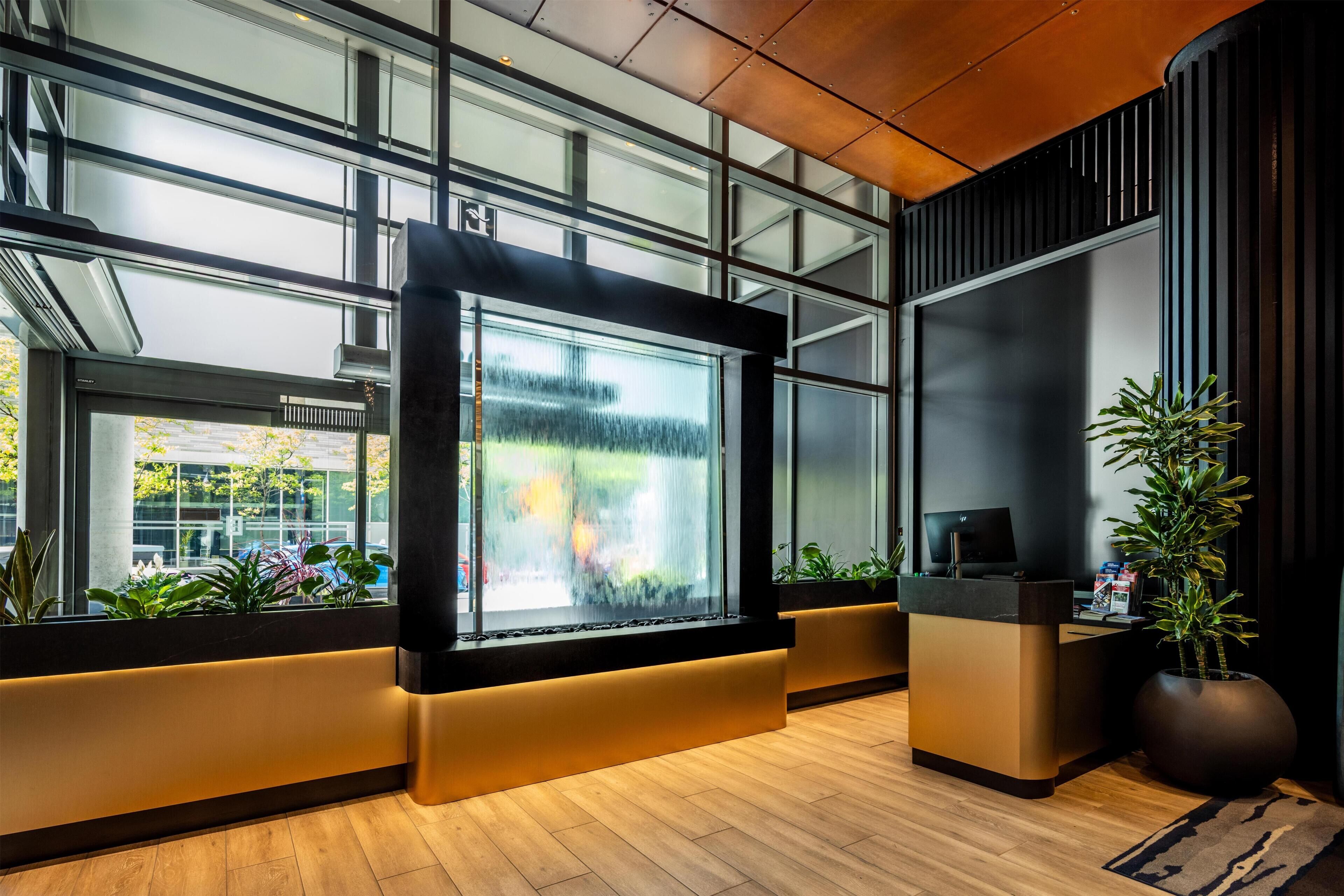 A modern interior with a large digital display, wooden flooring, and indoor plants.