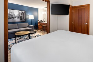 A hotel room with a bed, a sofa, a small round table, a bar area, and a television mounted on the wall. - Embassy Suites Montréal by Hilton (Montreal)