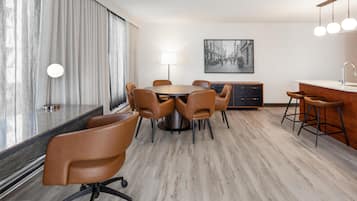 Una habitación de hotel moderna con zona de comedor, bar y un amplio ventanal con cortinas.