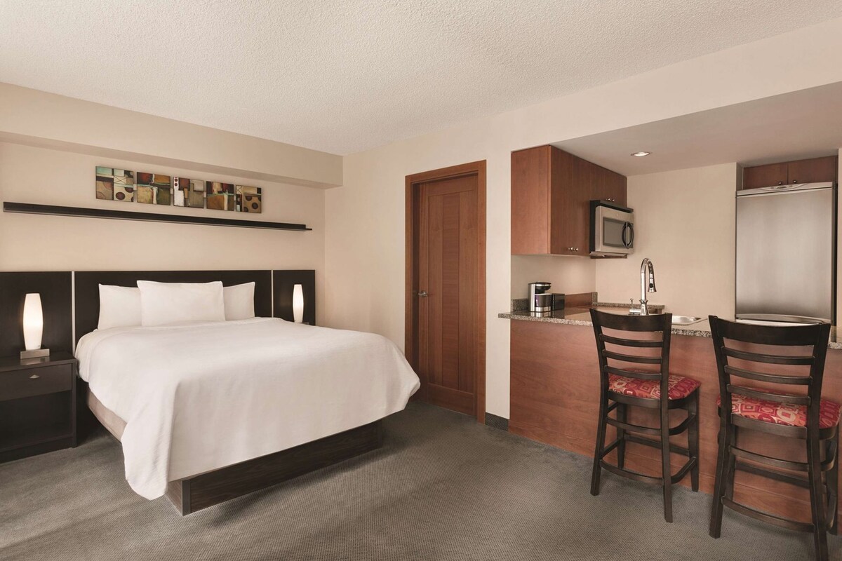 Quarto de hotel com cama, escrivaninha com duas cadeiras, micro-ondas e pia.