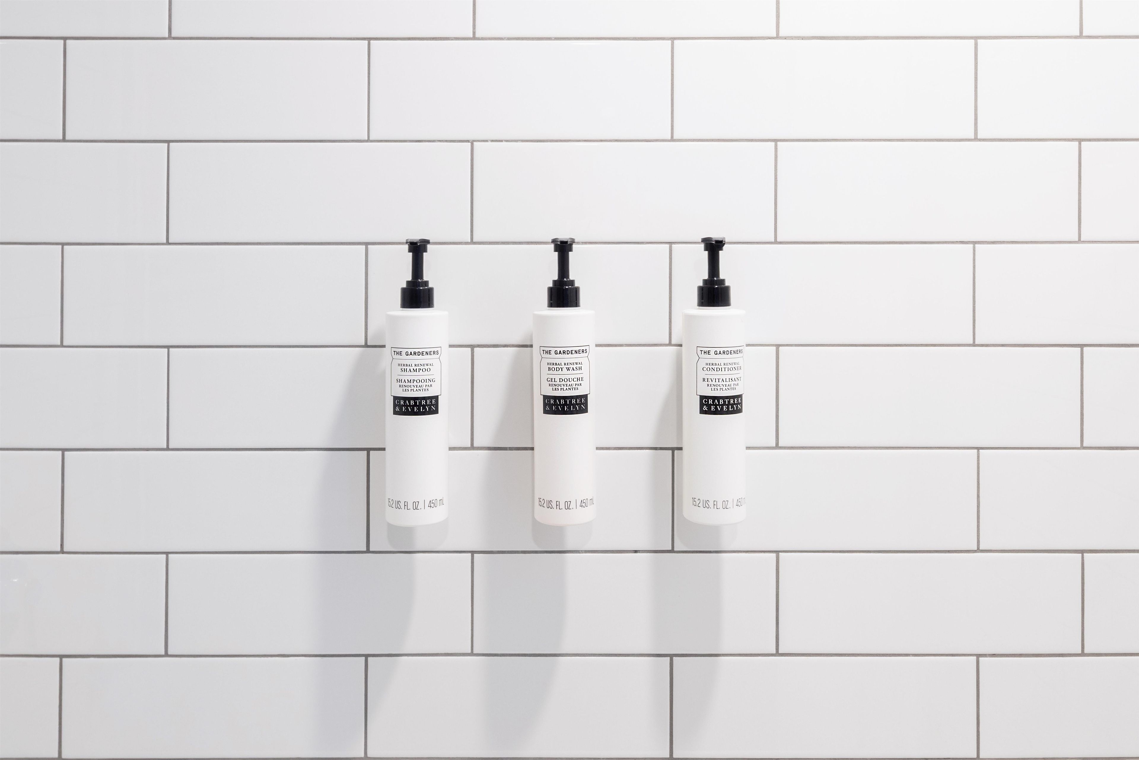 Three white bottles of The Gardeners brand products on a white tiled wall.